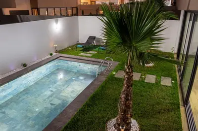a swimming pool with a palm tree in a building at Dar Bouazza Luxury apartment with pools garden sports courts parking near the sea in Dar Bouazza