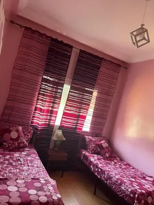 a bedroom with two beds and a window with blinds at Bel appartement in O Ben Slimane