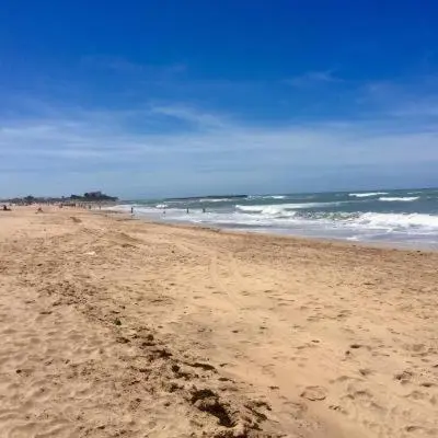 a sandy beach with people in the water and the ocean at Appartement à louer Aux perles de tamaris in Tamaris