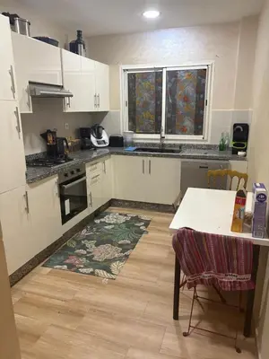 a kitchen with white cabinets and a table and a rug at Nice apartment with terrace overlooking pool in O Ben Slimane