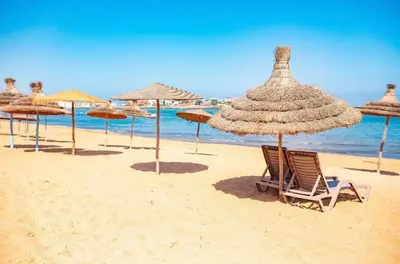 a group of straw umbrellas and chairs on a beach at Pearl Of Eden Island in Bouznika