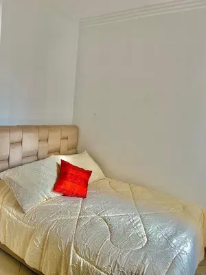 a bed with a red pillow on top of it at Zenata Family Apartment in Aïn Harrouda