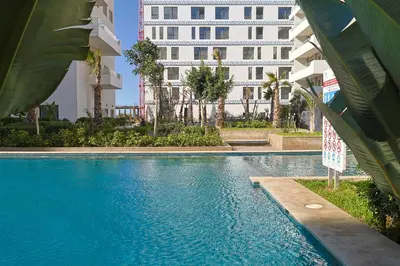 a swimming pool in front of a white building at Studio Cosy avec Piscine & proche de la plage in Aïn Harrouda