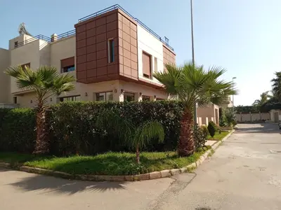 a building with palm trees in front of a street at Villa avec piscine proche de la mer in Mohammedia