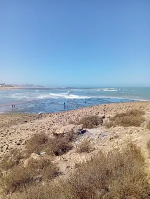 a beach with people walking on the sand and the ocean at Appartement familial à 100 m de la mer in El Harhoura