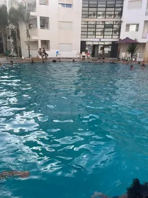 a swimming pool with blue water in front of a building at apartement avec piscine résidence sécurisée meublé confort jnan dalia Boznika in O Ben Slimane