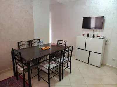a dining room with a table and a white refrigerator at Eco Gare centre 2 chambres in Bouznika