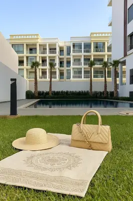 a straw hat and a purse sitting on a blanket in front of a building at Cozy & Chill à 30min terrain de foot Netflix, AC pool & beach 2 min, in Bouznika