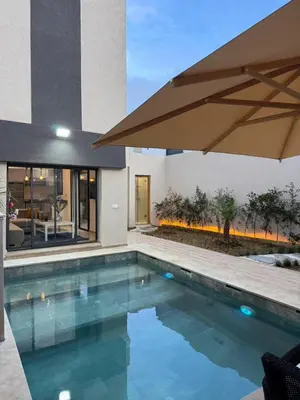 a swimming pool with an umbrella next to a house at Villa 2 Évasion Urbaine, 3 Chambres, à 20 min de Rabat in Sidi Yahia az Zaʼer