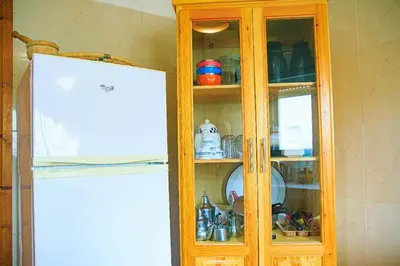 a wooden cabinet with dishes in it next to a refrigerator at CAN Comfort 2 Bedrooms in Temara
