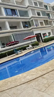 a swimming pool with two umbrellas and chairs and a building at Appt Mansbay beach in Mansouria