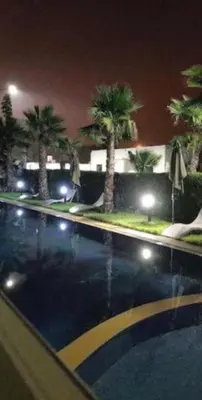 a swimming pool at night with palm trees and lights at Diha Appartement in Sidi Rahal