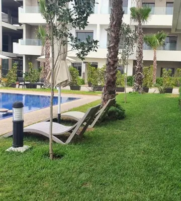 a resort pool with a hammock and palm trees at Diha Appartement in Sidi Rahal