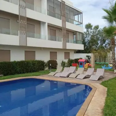 a building with a swimming pool with lounge chairs and a playground at Diha Appartement in Sidi Rahal