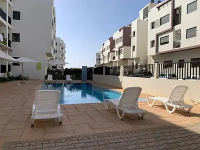 two chairs and a swimming pool in front of some buildings at Dar Lakbira Bouznika in Bouznika