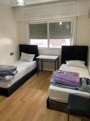 two beds in a room with a table and two windows at Casablanca B& in Casablanca
