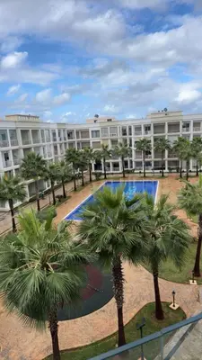 a large building with palm trees in front of it at Palm Pool View Apartment - Bouznika in Bouznika