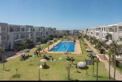 a group of people sitting around a swimming pool at Appartement Cosy avec Vue Piscine in Mansouria