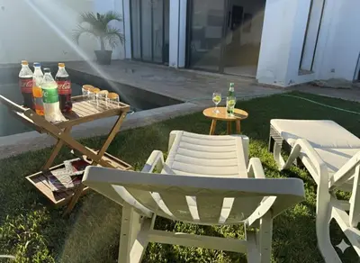 a patio with two chairs and a table with drinks at Grande villa sécurisée piscine privée in Dar Bouazza