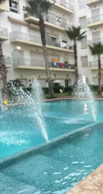 a fountain in a swimming pool in front of a building at 2 bedroom apartment in a secured residence, minutes to beach in Bouznika