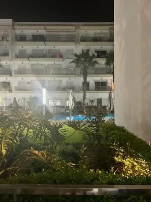 a building with a palm tree and a swimming pool at 2 bedroom apartment in a secured residence, minutes to beach in Bouznika