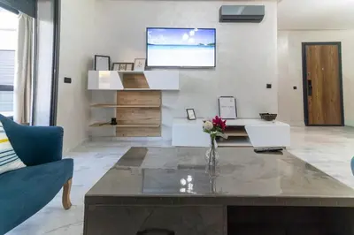 a living room with a table and a tv on the wall at Piscine Chauffée Salle de Sport Balcon Panoramique in Mohammedia