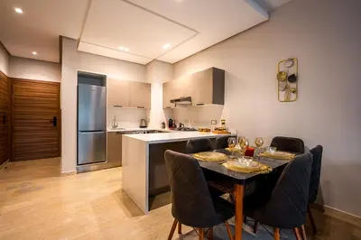 a kitchen with a table and chairs and a kitchen with a counter at L'Amber 1 chambre - 5 min de l'Aéroport- Piscine in Nouaseur