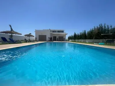 a large blue swimming pool in front of a house at Riad El menez in Bouznika