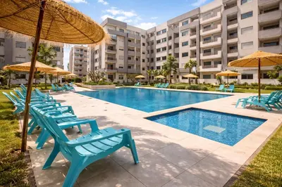 a swimming pool with blue chairs and umbrellas at Modern Cozy Apartment in Prime Location in Nouaceur