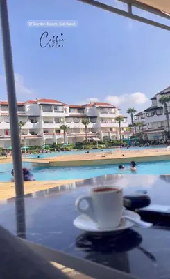 a cup of coffee sitting on a table next to a swimming pool at Garden Beach in Sidi Rahal