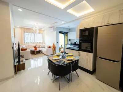 a kitchen and living room with a table and a refrigerator at Bel appartement, piscine intérieure et extérieure in Temara