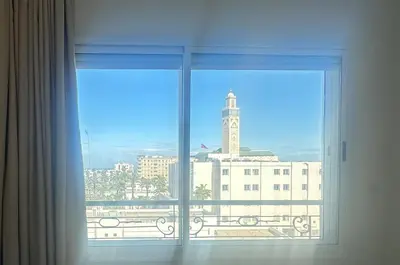 a window with a view of a building and a clock tower at Central Flat Corniche Casablanca in Casablanca