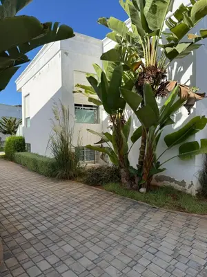 a white building with two trees next to a sidewalk at Bungalow à 1 minute de la plage in Rabat