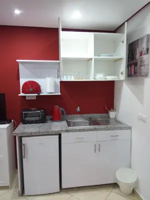 a small kitchen with white cabinets and a red wall at Studios Taha in Rabat