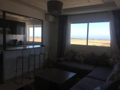 a living room with a couch and a table and a kitchen at DaliMAR in Bouznika