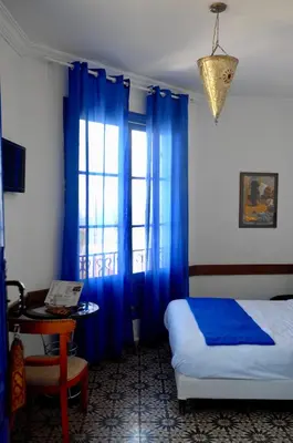 a bedroom with blue curtains and a bed and a table at Hôtel Central in Casablanca