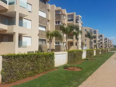 an apartment building with palm trees and a sidewalk at Evasion Bouznika أمام شاطىء بوزنيقة in Bouznika