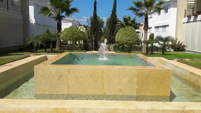a fountain in the middle of a park with palm trees at Les perles de tamaris dar bouazza in Dar Mohammed Ould Haj Jilali