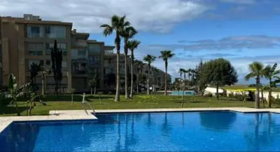 a large blue swimming pool with palm trees and buildings at appartments front mer in Bouznika
