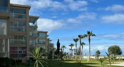 a building with palm trees in front of a beach at appartments front mer in Bouznika