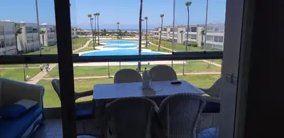 a table with chairs and a view of a pool from a window at Ola Blanca 1 in Dar Hamida