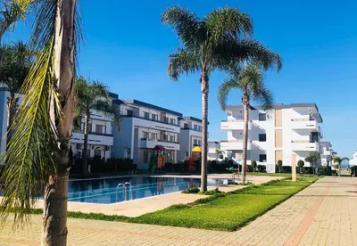 a swimming pool with palm trees in front of a building at Marbella Beach location pour famille 2 chambres in Mansouria