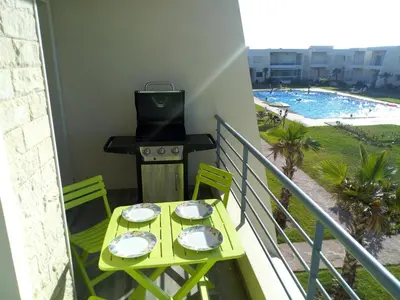 a balcony with a table with a grill and a pool at Savannah Beach D11 in Sidi Rahal