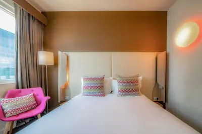 a bedroom with a large bed and a pink chair at Campanile Casablanca Centre Ville in Casablanca