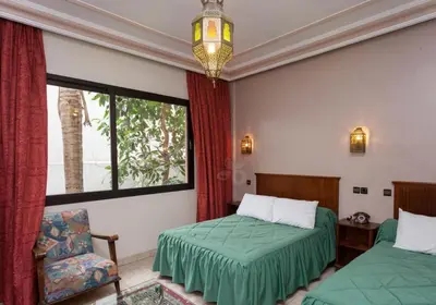 a bedroom with two beds and a chair and a window at Hôtel Astrid in Casablanca