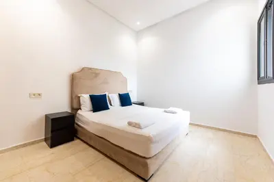 a white bedroom with a large bed with blue pillows at Garden Bay Appart'Hôtel in Casablanca