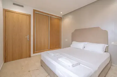 a bedroom with a large white bed and a wooden door at Garden Bay Appart'Hôtel in Casablanca