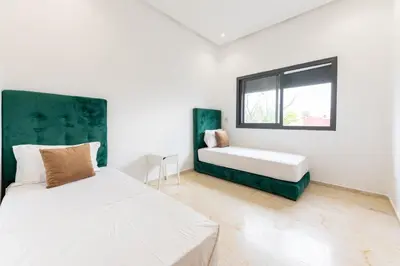 a white bedroom with a bed and a window at Garden Bay Appart'Hôtel in Casablanca