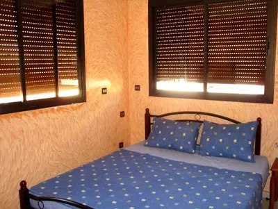 a bedroom with a bed with blue sheets and two windows at Silia Appartements in Temara