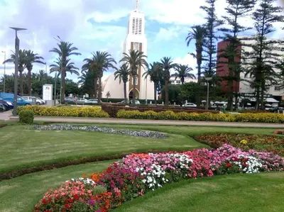 a building with a clock tower and flowers in a park at Très bel appartement en face du parc, près du Novotel in Mohammedia